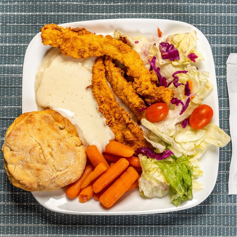 Fried chicken strips with gravy, a biscuit, baby carrots, and a side salad with cherry tomatoes.